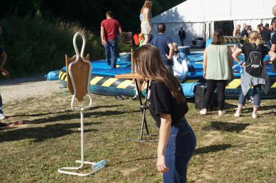 Un grand groupe de jeunes assis dehors sur un sol en béton, près de bâtiments sous un ciel nuageux.
