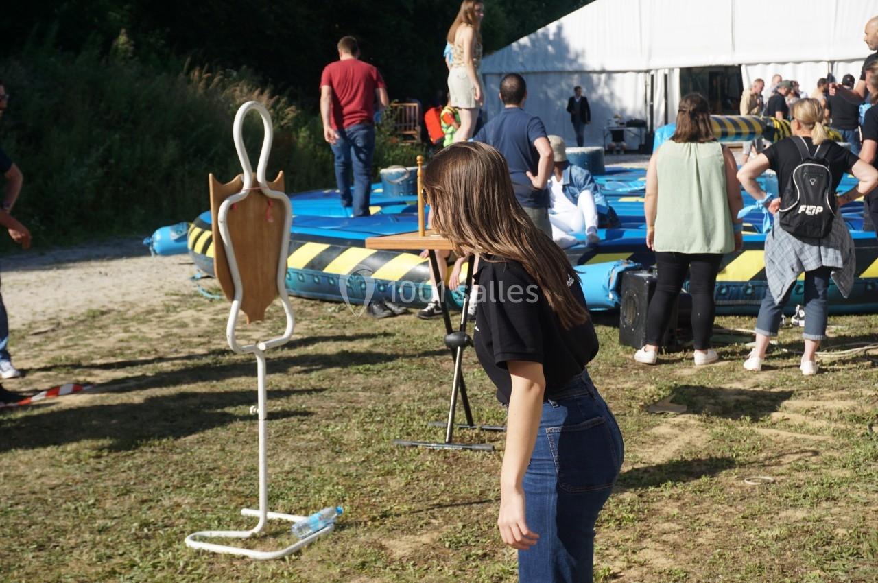 Une femme joue à un jeu d'adresse en extérieur, visant une chaise en bois montée sur un support.