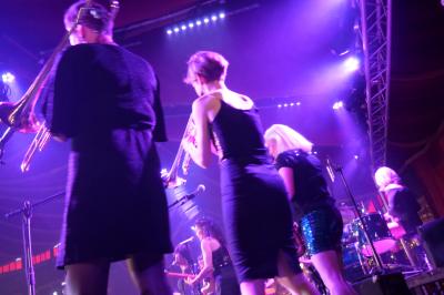Un grand groupe de jeunes assis dehors sur un sol en béton, près de bâtiments sous un ciel nuageux.
