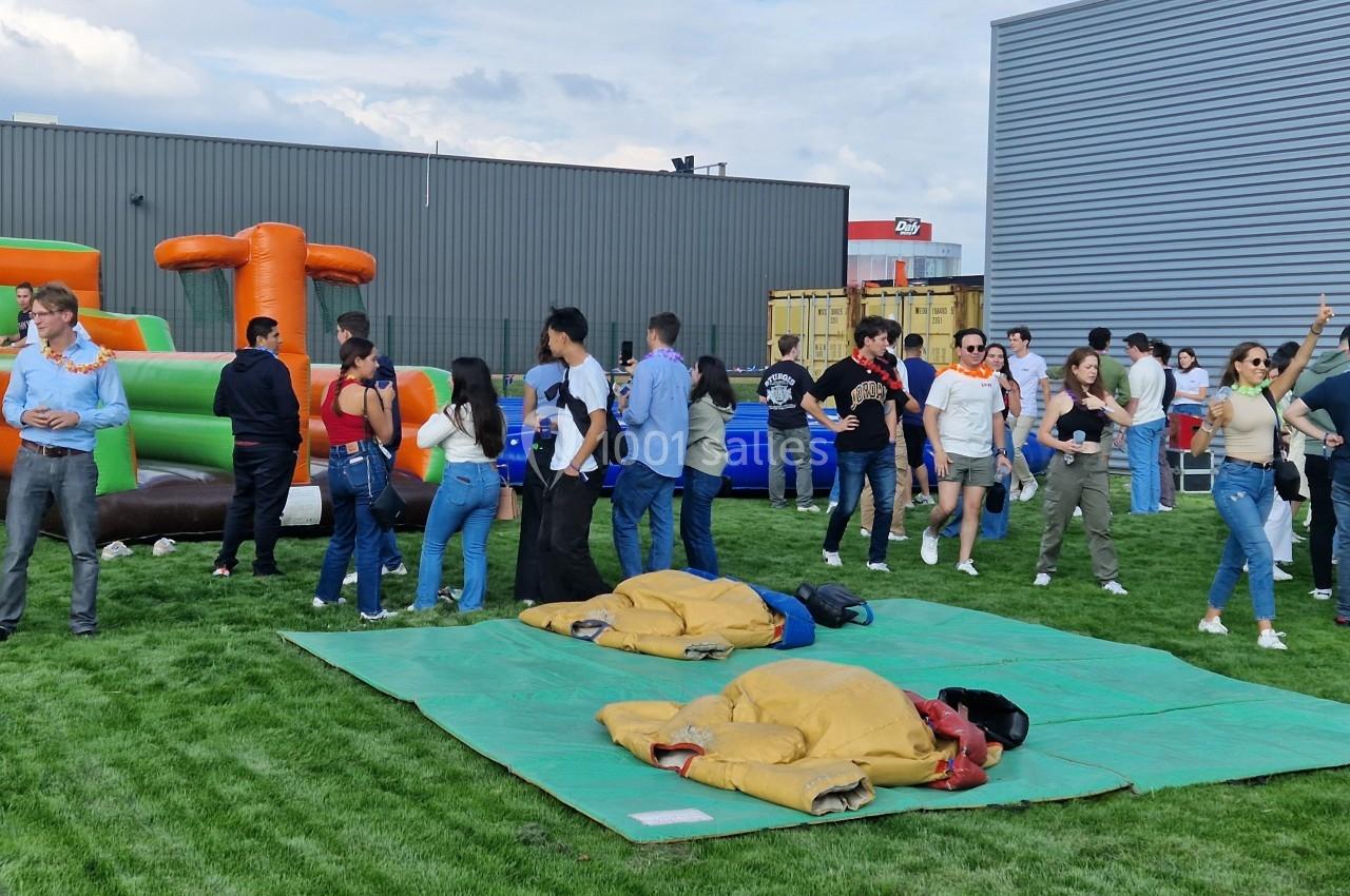 Des personnes participent à un événement en plein air avec des structures gonflables et des costumes de sumo sur une pelouse.