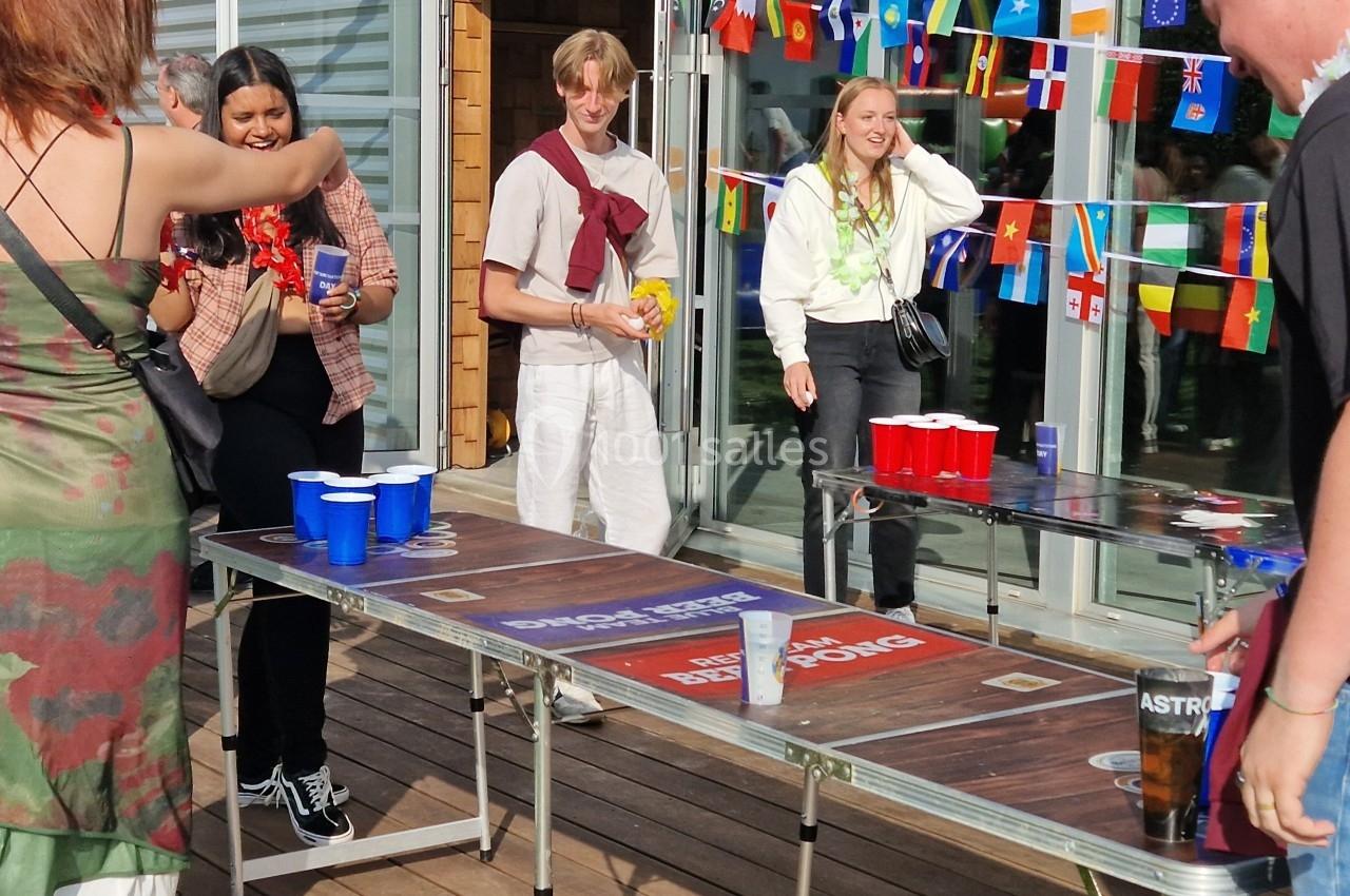Des personnes jouent au beer pong sur une terrasse, entourées de décorations avec des drapeaux internationaux.