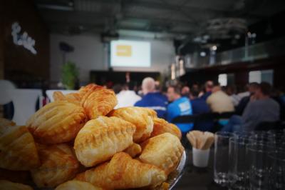 Un grand groupe de jeunes assis dehors sur un sol en béton, près de bâtiments sous un ciel nuageux.