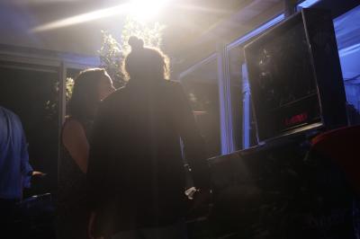 Un grand groupe de jeunes assis dehors sur un sol en béton, près de bâtiments sous un ciel nuageux.