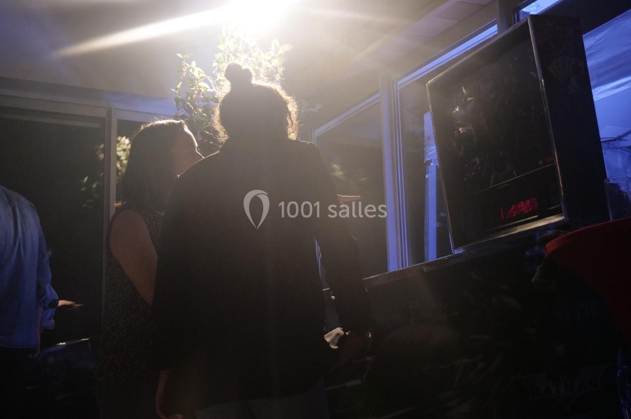 Deux personnes jouent à un flipper dans un espace faiblement éclairé avec des reflets lumineux.