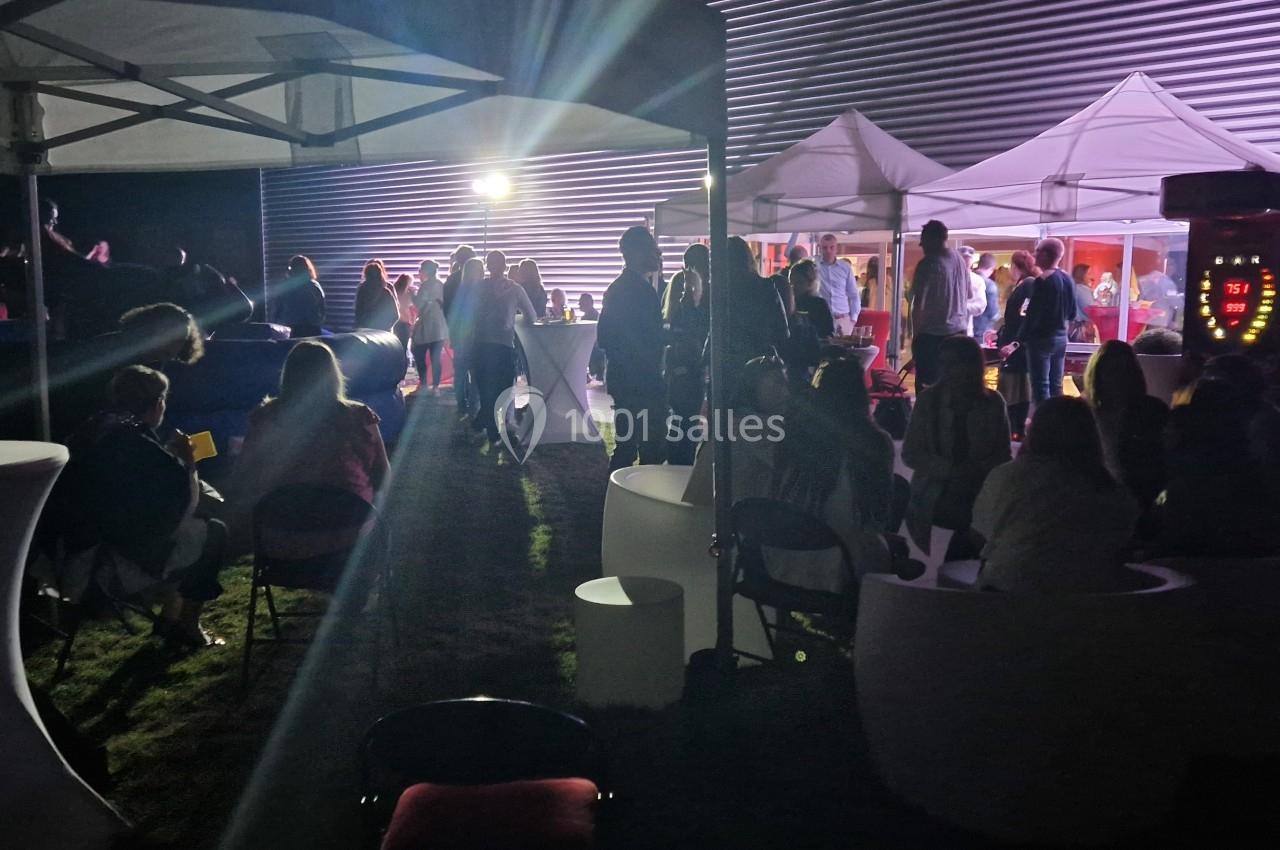 Groupe de personnes rassemblées sous des tentes éclairées la nuit, dans une ambiance festive en extérieur.