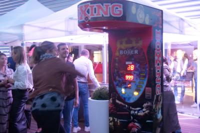 Un grand groupe de jeunes assis dehors sur un sol en béton, près de bâtiments sous un ciel nuageux.