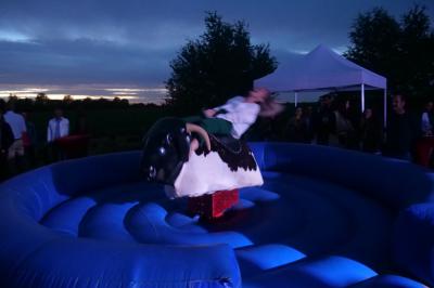 Un grand groupe de jeunes assis dehors sur un sol en béton, près de bâtiments sous un ciel nuageux.