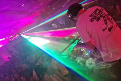 Un grand groupe de jeunes assis dehors sur un sol en béton, près de bâtiments sous un ciel nuageux.