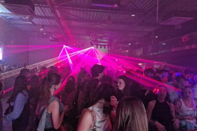 Un grand groupe de jeunes assis dehors sur un sol en béton, près de bâtiments sous un ciel nuageux.