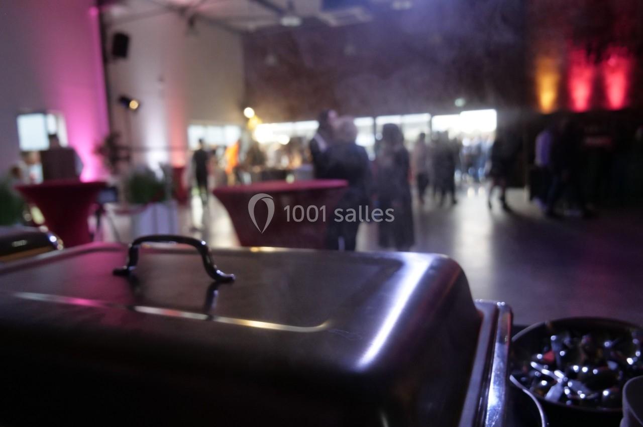 Vue floue d'une salle événementielle éclairée, avec un buffet au premier plan et des invités en arrière-plan.