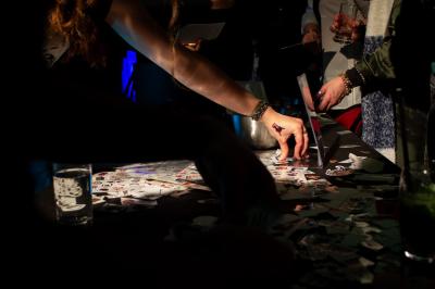 Un grand groupe de jeunes assis dehors sur un sol en béton, près de bâtiments sous un ciel nuageux.