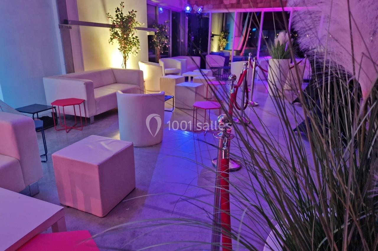 Espace lounge avec fauteuils blancs, tables basses et plantes, éclairé par des lumières colorées dans une ambiance nocturne.