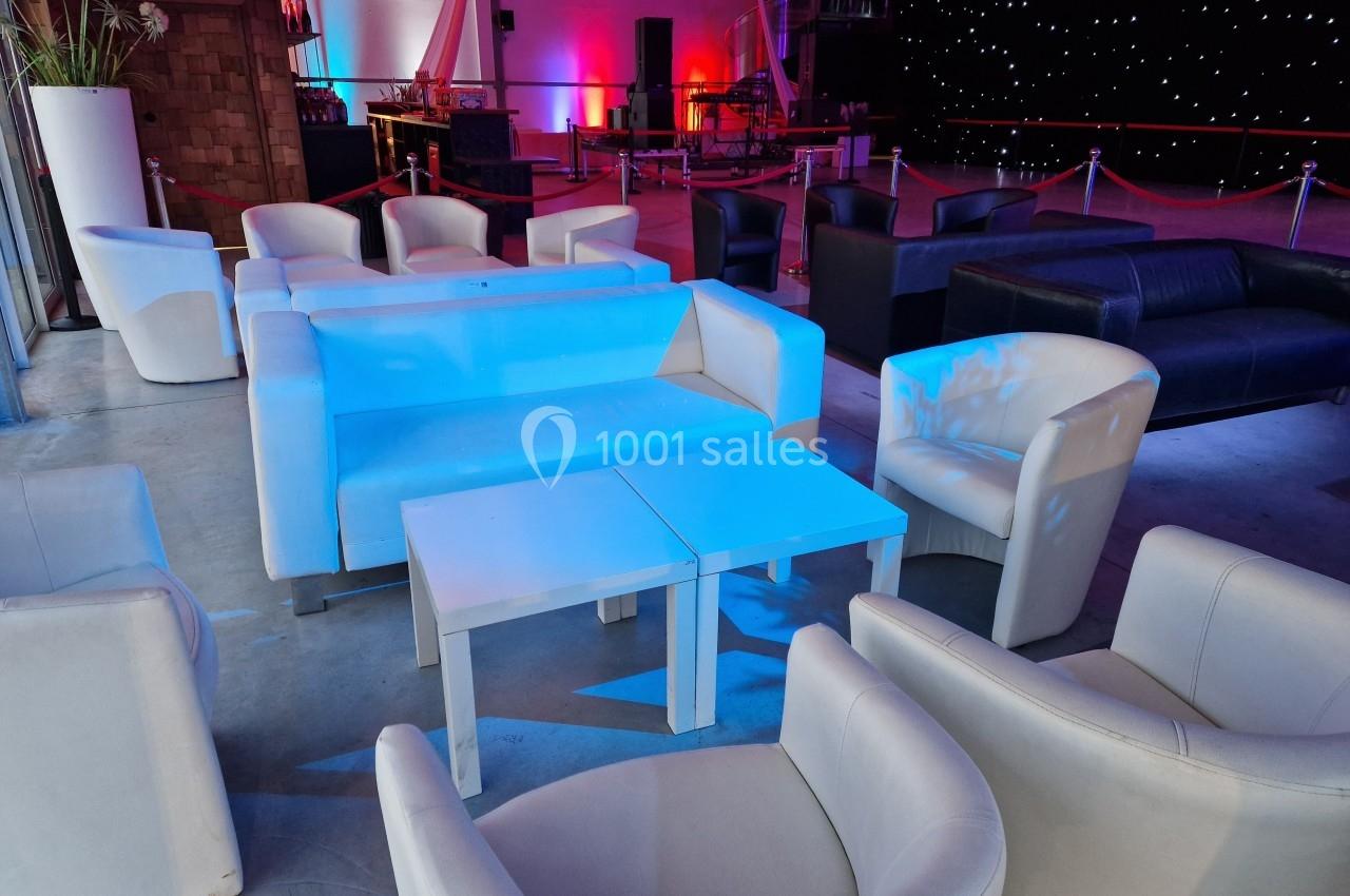 Fauteuils et canapés blancs disposés autour de tables basses dans une salle éclairée par des lumières colorées.