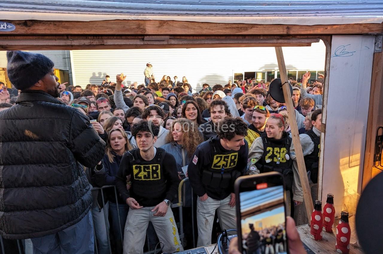 Un groupe de personnes rassemblées devant une scène en plein air, écoutant un intervenant avec un micro.