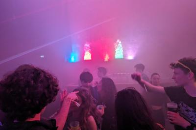Un grand groupe de jeunes assis dehors sur un sol en béton, près de bâtiments sous un ciel nuageux.