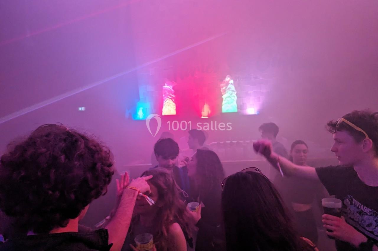 Des personnes dansent et discutent dans une ambiance de fête avec éclairages colorés et fumée.