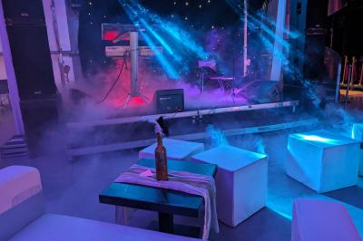 Un grand groupe de jeunes assis dehors sur un sol en béton, près de bâtiments sous un ciel nuageux.