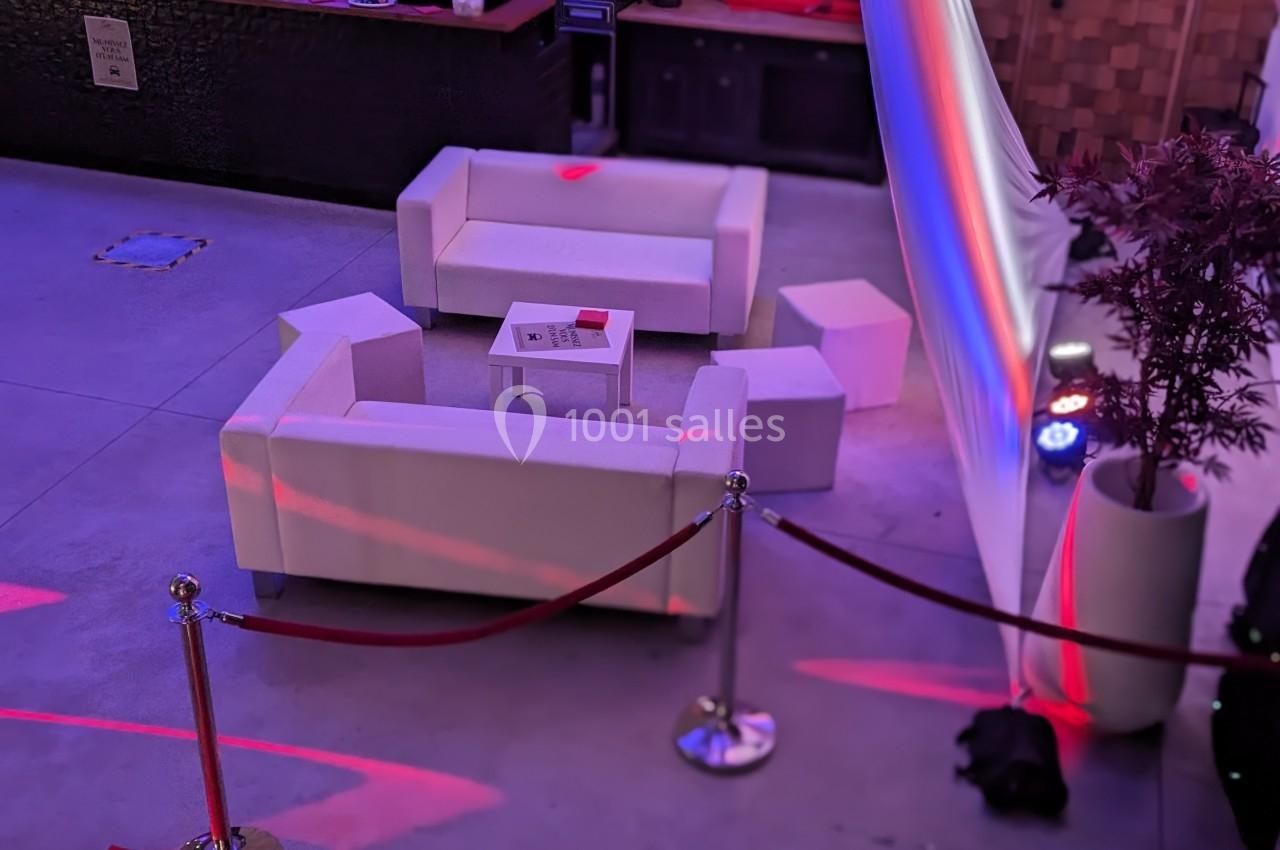 Espace lounge avec canapés blancs disposés autour d'une table basse, délimité par des cordons rouges.