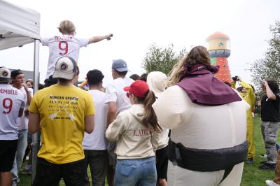 Un grand groupe de jeunes assis dehors sur un sol en béton, près de bâtiments sous un ciel nuageux.