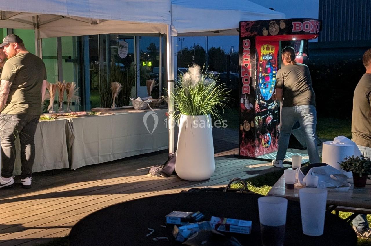 Un homme frappe une machine de boxe sous une tente lors d'un événement en plein air, avec des tables et décorations autour.