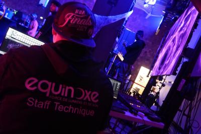 Un grand groupe de jeunes assis dehors sur un sol en béton, près de bâtiments sous un ciel nuageux.
