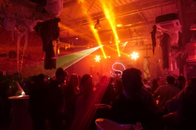 Un grand groupe de jeunes assis dehors sur un sol en béton, près de bâtiments sous un ciel nuageux.
