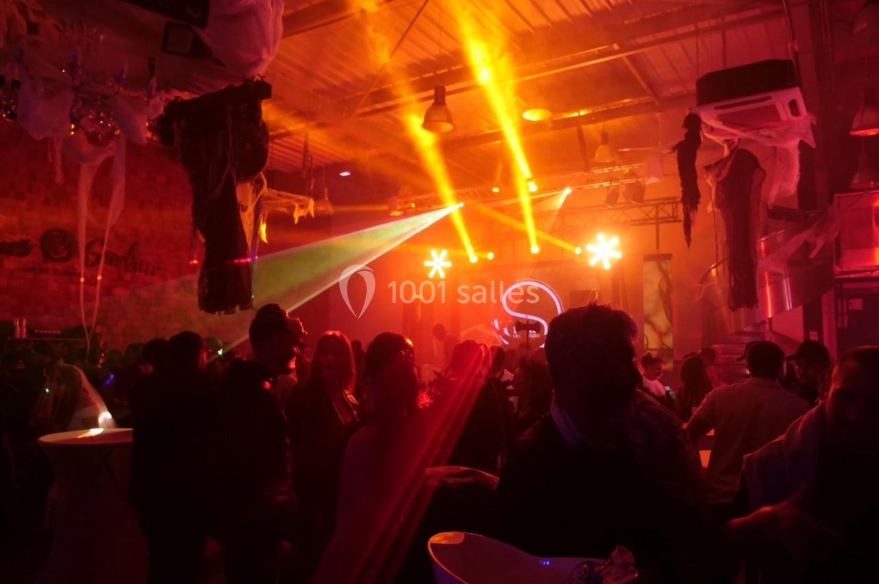 Salle de fête animée avec des lumières colorées, des invités debout et une scène éclairée en arrière-plan.