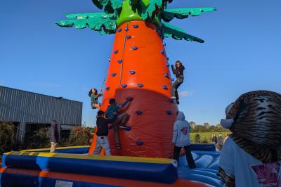 Un grand groupe de jeunes assis dehors sur un sol en béton, près de bâtiments sous un ciel nuageux.