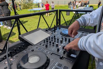 Un grand groupe de jeunes assis dehors sur un sol en béton, près de bâtiments sous un ciel nuageux.