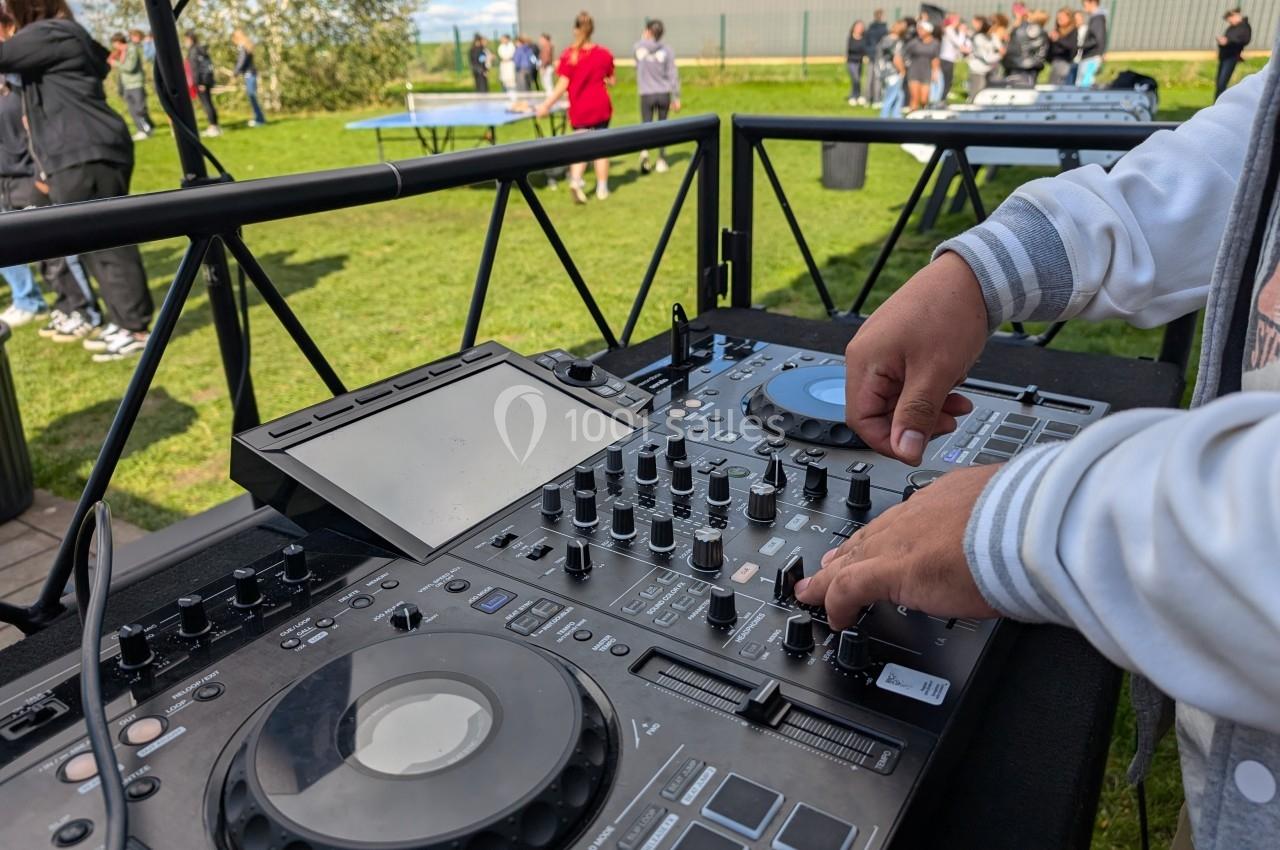 Une personne utilise une table de mixage lors d'un événement en plein air avec des participants en arrière-plan.