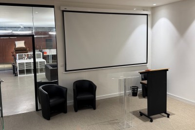 Un grand groupe de jeunes assis dehors sur un sol en béton, près de bâtiments sous un ciel nuageux.