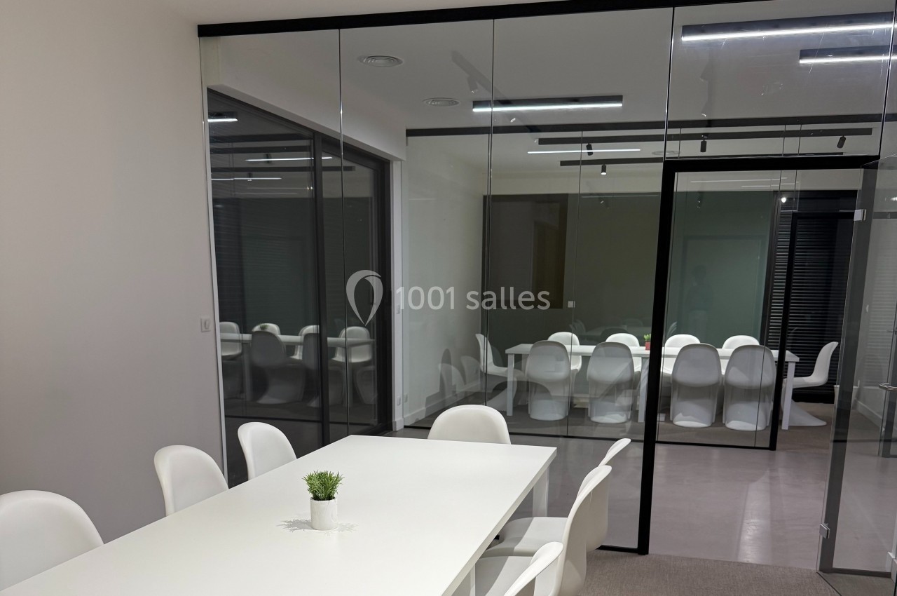 Salle de réunion moderne avec murs vitrés, table blanche, chaises assorties et petite plante décorative.