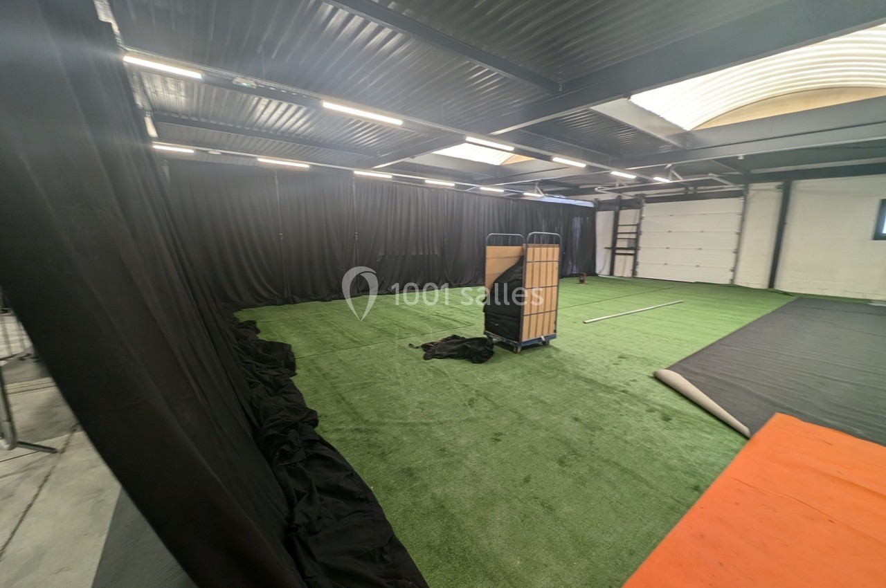 Salle intérieure avec sol en gazon synthétique, rideaux noirs, éclairage au plafond et matériel de rangement au centre.