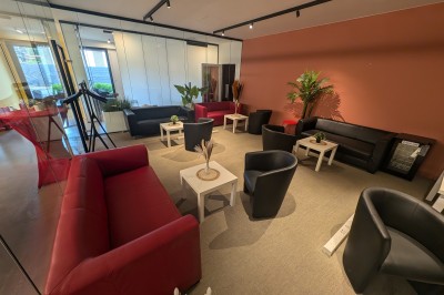 Un grand groupe de jeunes assis dehors sur un sol en béton, près de bâtiments sous un ciel nuageux.