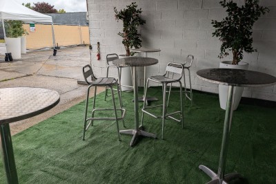 Un grand groupe de jeunes assis dehors sur un sol en béton, près de bâtiments sous un ciel nuageux.