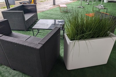 Un grand groupe de jeunes assis dehors sur un sol en béton, près de bâtiments sous un ciel nuageux.