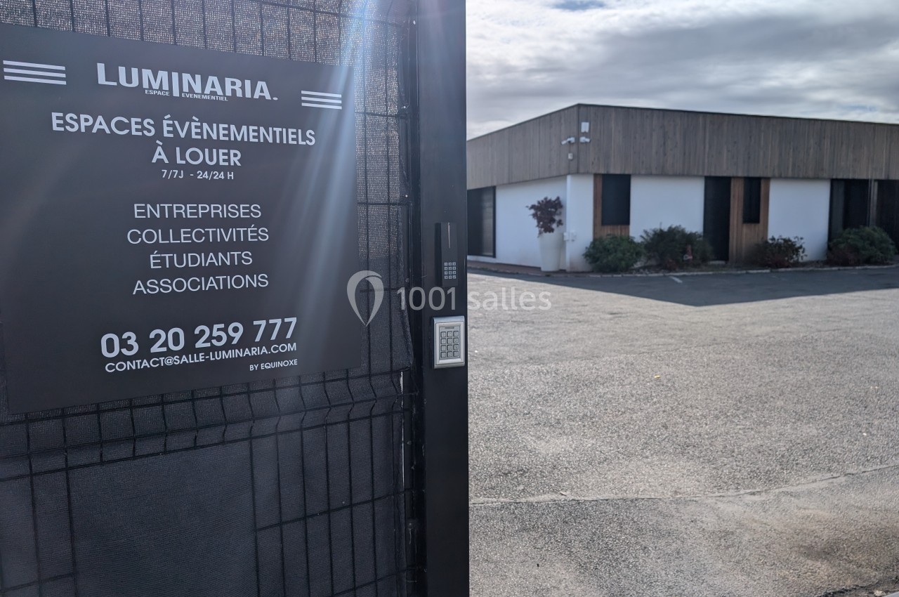 Vue d'une entrée clôturée avec un panneau indiquant des espaces événementiels à louer, bâtiment en arrière-plan.