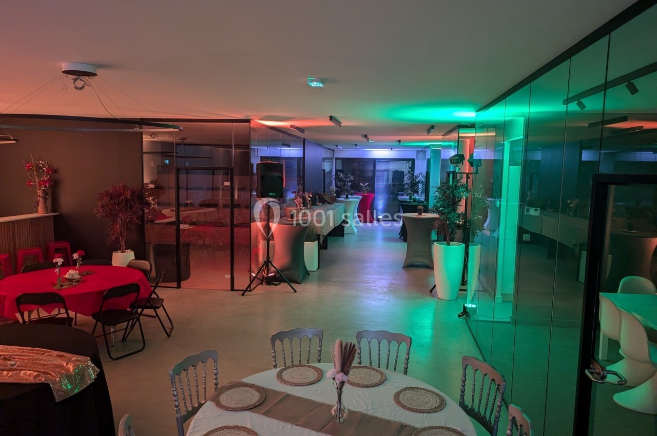 Salle de réception moderne avec tables dressées, éclairage coloré et espace buffet en arrière-plan.