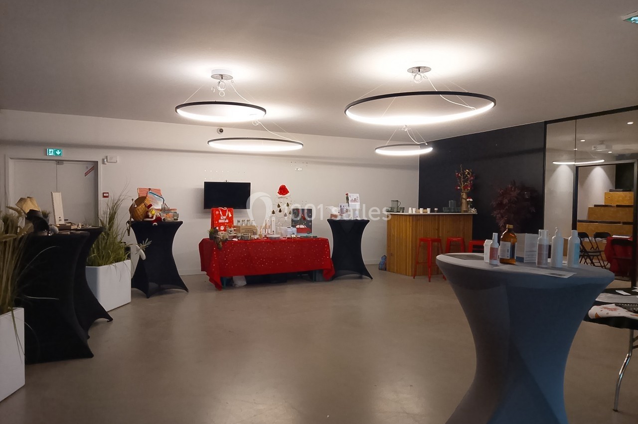 Salle aménagée avec des tables hautes, un stand décoré de Noël et un éclairage moderne suspendu.