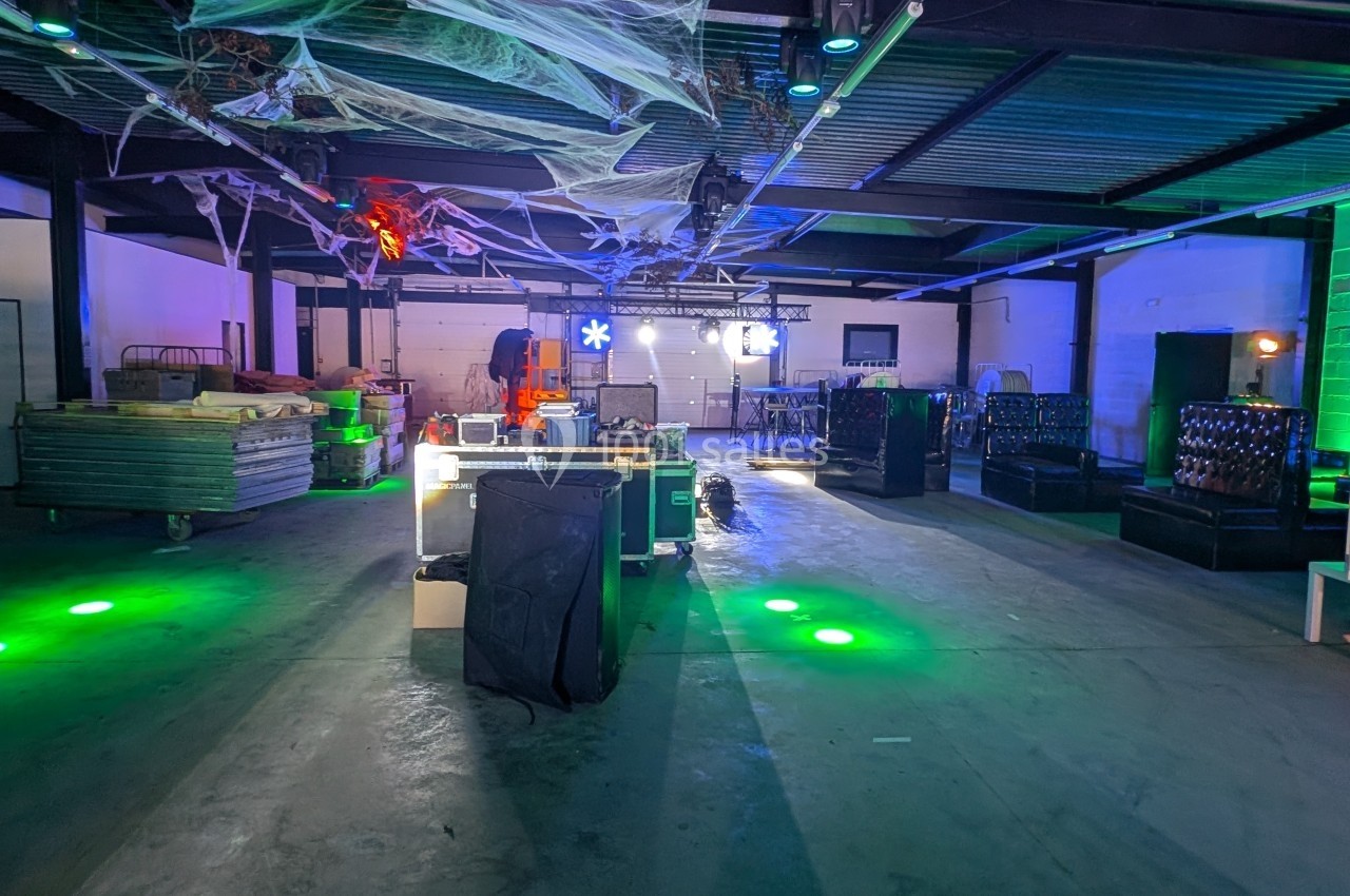 Entrepôt décoré pour un événement avec éclairage coloré, toiles d'araignée suspendues et mobilier disposé.