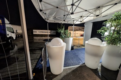 Des enfants colorient des dessins autour d'une table ronde, entourés d'adultes dans un espace intérieur animé.