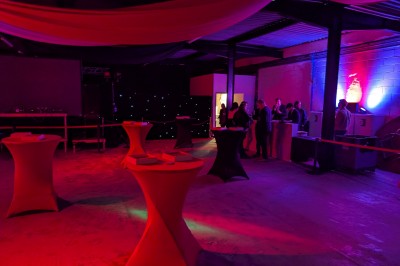 Des enfants colorient des dessins autour d'une table ronde, entourés d'adultes dans un espace intérieur animé.