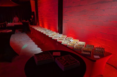 Des enfants colorient des dessins autour d'une table ronde, entourés d'adultes dans un espace intérieur animé.