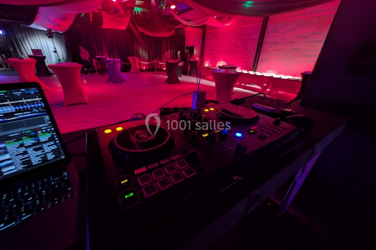 Console de mixage DJ en premier plan dans une salle décorée de lumières rouges et violettes pour un événement.