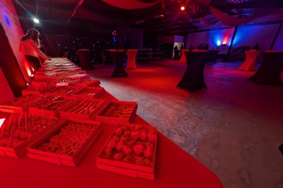 Des enfants colorient des dessins autour d'une table ronde, entourés d'adultes dans un espace intérieur animé.