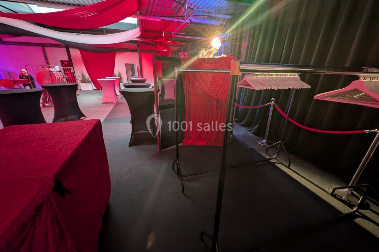 Salle décorée avec des tissus rouges et noirs, portant des portants à vêtements et des tables hautes drapées.