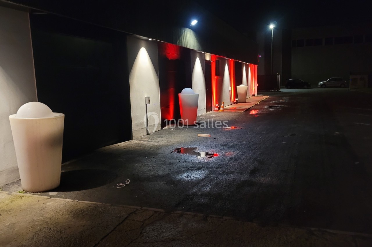 Allée sombre éclairée par des lumières rouges et blanches, avec des bornes lumineuses et des flaques d'eau au sol.