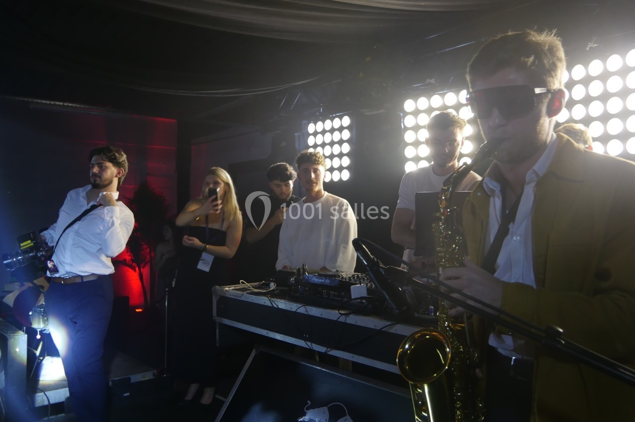 Un groupe de musiciens et un DJ jouent sur scène, éclairés par des lumières vives dans une ambiance festive.