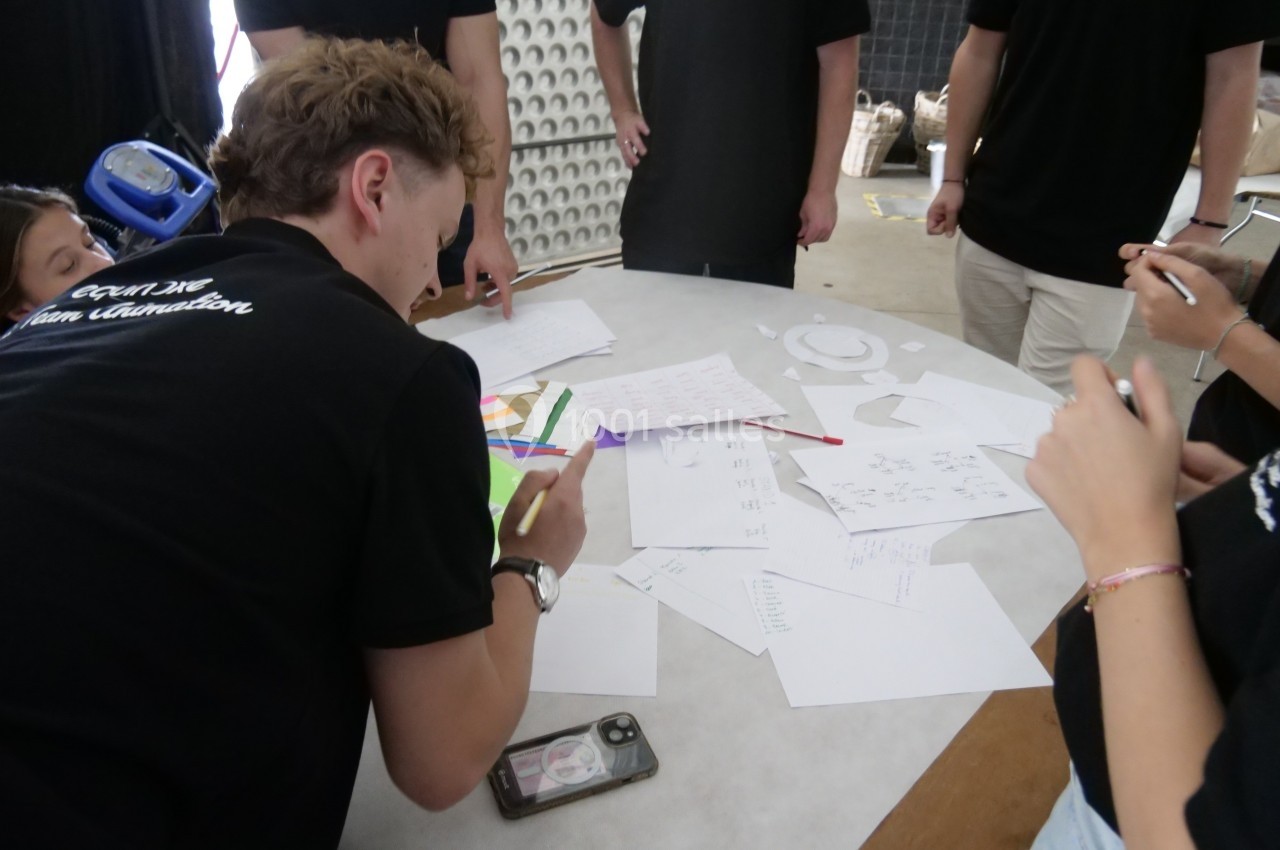 Des personnes collaborent autour d'une table recouverte de feuilles, schémas et dessins dans un environnement intérieur.