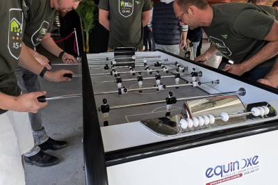 Des enfants colorient des dessins autour d'une table ronde, entourés d'adultes dans un espace intérieur animé.